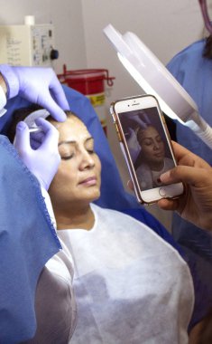 Doktor bir şırınga ile cilt üzerinde estetik bir tedavi yapan, birkaç öğrenci cep telefonu ile prosedür kayıt ise