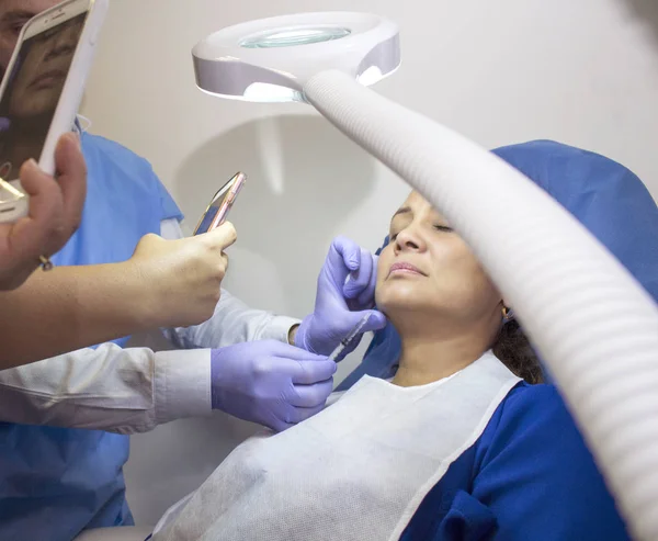 under the light of a lamp, a doctor performs an aesthetic treatment while several students record with their cell phone