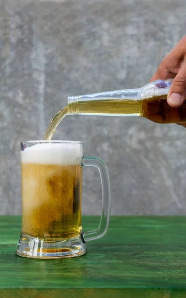 Serving beer foaming in a jug on a green wooden table
