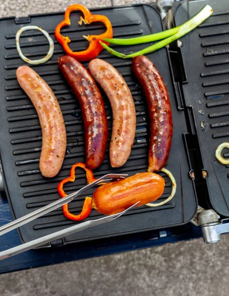 Close-up of a sausage caught with a clamp with a bottom of a grill with unfocused sausages — Stock Photo, Image