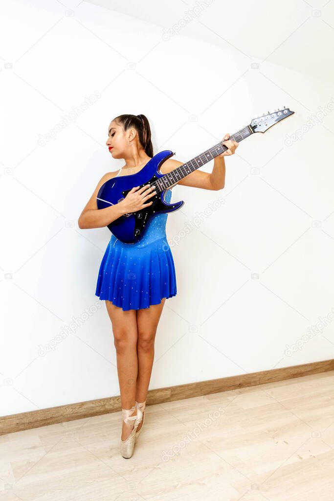 Teen girl in elegant ballet position standing on the tips of her dance shoes playing an electric guitar in her living room