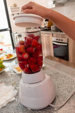 Bir kadının eli ev mutfağında blender 'da çilek suyu hazırlıyor.