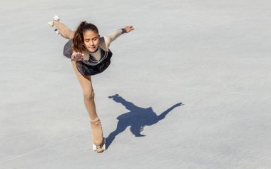 Kahverengi tenli genç kız tekerlekli sandalyede artistik patinaj yapıyor. Güvercin figürü