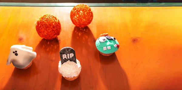 cup cakes with Halloween characters on a wooden background with copyspace. Ghost, tombstone, monster, shadows
