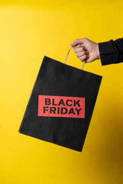 Customer holding shopping bag with black friday inscription on yellow background