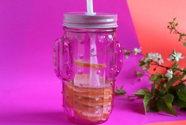 Koyu pembe arka plan ve arka planda yeşil bir dal üzerinde bir kokteyl tüp ile bir kaktüs şeklinde pembe cam.