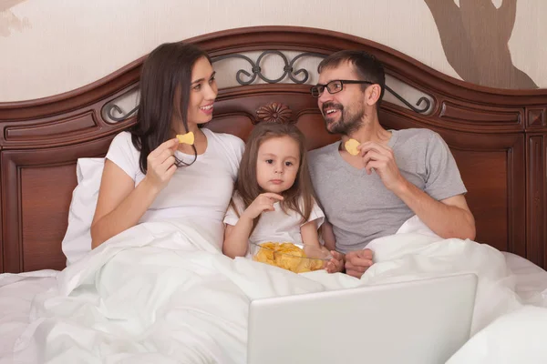 Mutlu aile yatakta film izlerken ve cips yemek.