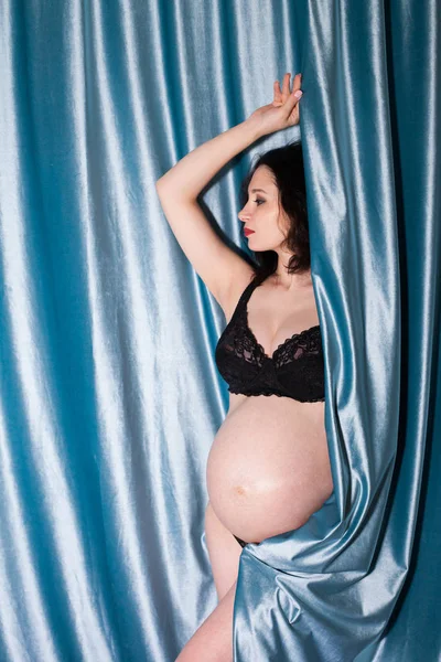Pregnant girl on a background of blue curtains
