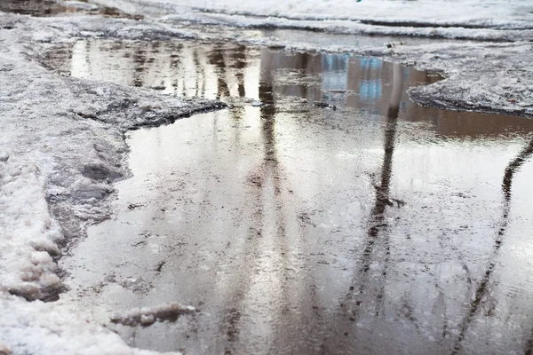 Deep puddle with lumps snow melts on the road in the city, during the melting of snow