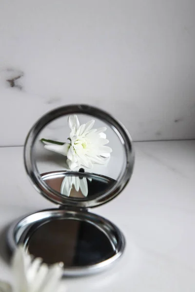 White flower is reflected in the mirror on light marble background. Beauty concept