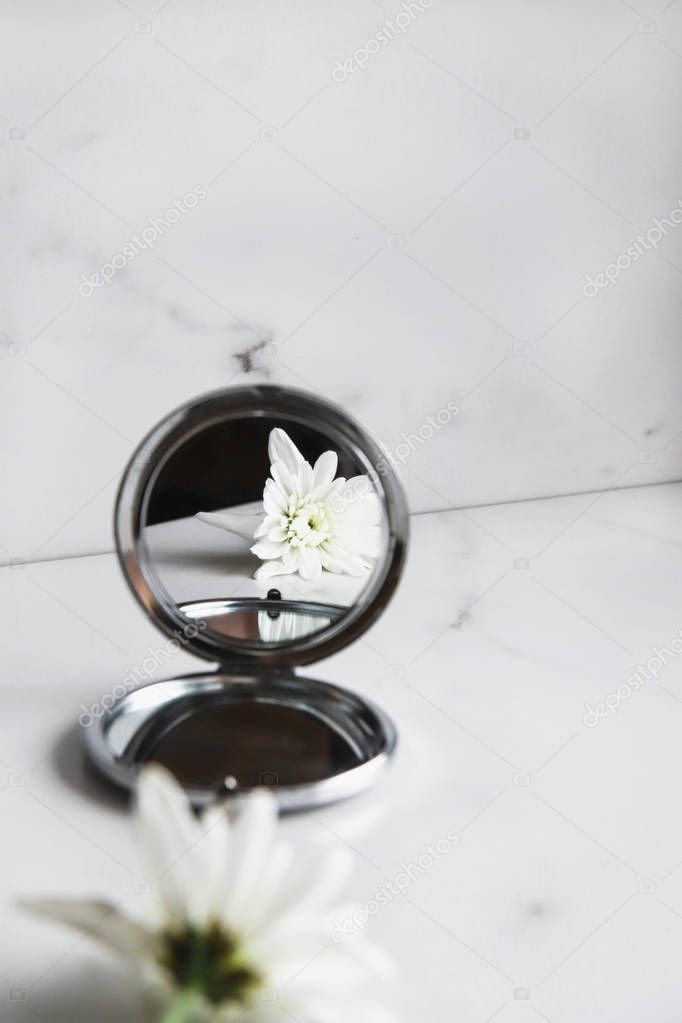 White flower is reflected in the mirror on light marble background. Beauty concept