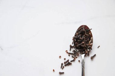 Gri mermer arka planda kaşık içinde kurumuş karanfiller. Sıcak çay, kış içecekleri ve yemek için baharat. Kapat ve üst görünüm