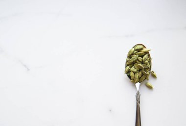 Kaşık içinde kakule tohumları. Yeşil ve sağlıklı baharat konsepti. Yiyecek ve içecek çeşnisi. Üst görünüm ve düz uzanma