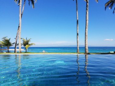 Bir tatil Bali, Endonezya Candidasa plajda Hint Okyanusu'na bakan bir sonsuzluk havuzunda yansıyan palmiye ağaçları