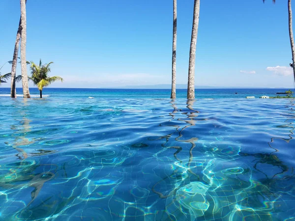 Bir tatil Bali, Endonezya Candidasa plajda Hint Okyanusu'na bakan bir sonsuzluk havuzunda yansıyan palmiye ağaçları
