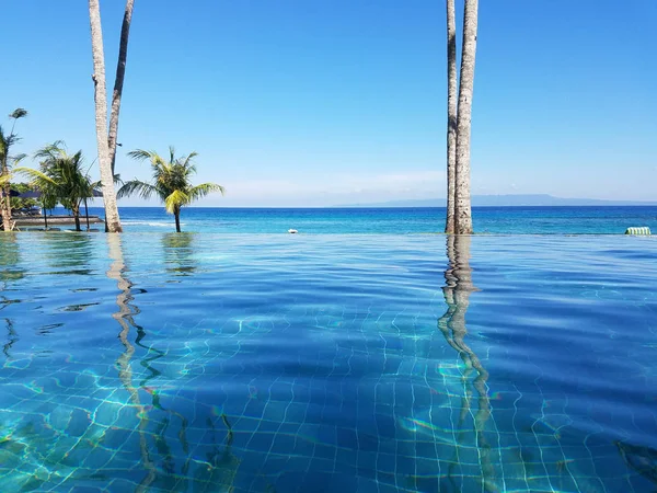 Bir tatil Bali, Endonezya Candidasa plajda Hint Okyanusu'na bakan bir sonsuzluk havuzunda yansıyan palmiye ağaçları