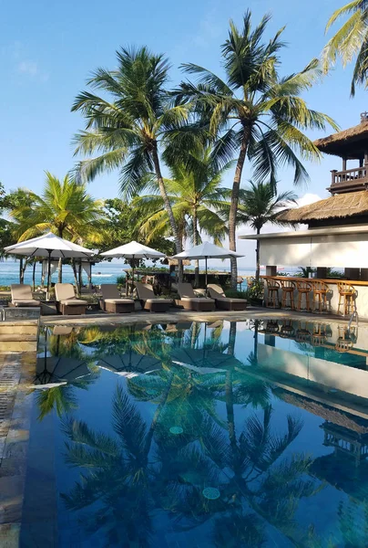 Pool and bar amenities surrounded by palm trees, in a beach resort in Bali, Indonesia, for travel backgrounds.