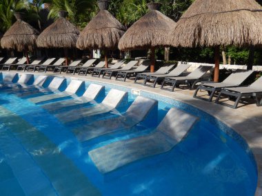 Oturma alanı ile saman şemsiye, şezlong sandalye ve palmiye ağaçları manzara, Cancun, Meksika için Riviera Maya üzerinde bir Caribbean beach Resort havuz.