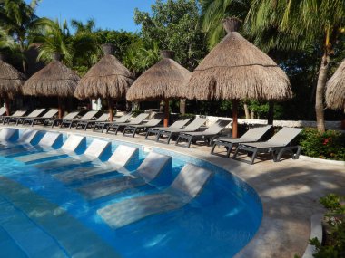 Oturma alanı ile saman şemsiye, şezlong sandalye ve palmiye ağaçları manzara, Cancun, Meksika için Riviera Maya üzerinde bir Caribbean beach Resort havuz.