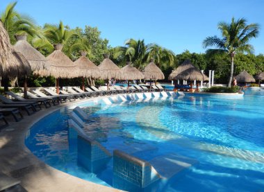 Oturma alanı ile saman şemsiye, şezlong sandalye ve palmiye ağaçları manzara, Cancun, Meksika için Riviera Maya üzerinde bir Caribbean beach Resort havuz.