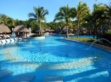 Oturma alanı ile saman şemsiye, şezlong sandalye ve palmiye ağaçları manzara, Cancun, Meksika için Riviera Maya üzerinde bir Caribbean beach Resort havuz.