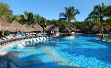 Oturma alanı ile saman şemsiye, şezlong sandalye ve palmiye ağaçları manzara, Cancun, Meksika için Riviera Maya üzerinde bir Caribbean beach Resort havuz.