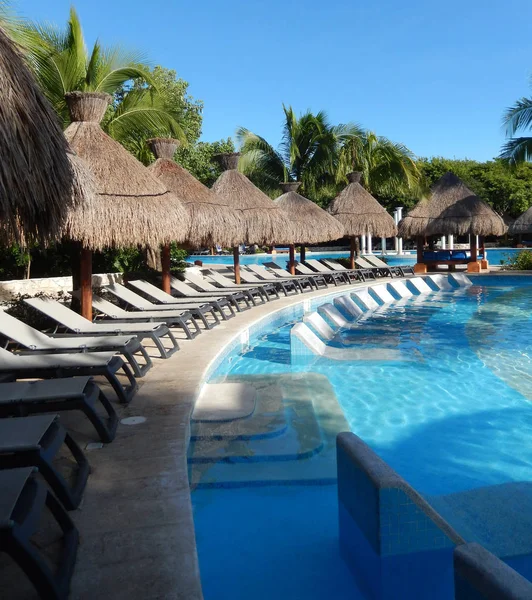 Oturma alanı ile saman şemsiye, şezlong sandalye ve palmiye ağaçları manzara, Cancun, Meksika için Riviera Maya üzerinde bir Caribbean beach Resort havuz.