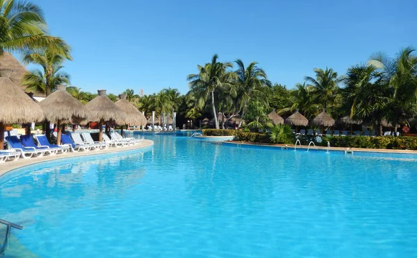 Oturma alanı ile saman şemsiye, şezlong sandalye ve palmiye ağaçları manzara, Cancun, Meksika için Riviera Maya üzerinde bir Caribbean beach Resort havuz.