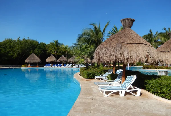 Oturma alanı ile saman şemsiye, şezlong sandalye ve palmiye ağaçları manzara, Cancun, Meksika için Riviera Maya üzerinde bir Caribbean beach Resort havuz.