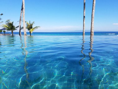 Bir tatil Bali, Endonezya Candidasa plajda Hint Okyanusu'na bakan bir sonsuzluk havuzunda yansıyan palmiye ağaçları