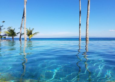 Bir tatil Bali, Endonezya Candidasa plajda Hint Okyanusu'na bakan bir sonsuzluk havuzunda yansıyan palmiye ağaçları