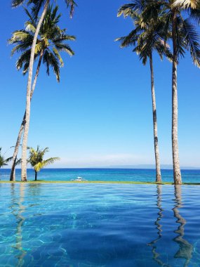 Bir tatil Bali, Endonezya Candidasa plajda Hint Okyanusu'na bakan bir sonsuzluk havuzunda yansıyan palmiye ağaçları