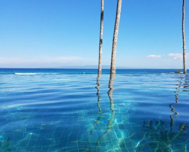 Bir tatil Bali, Endonezya Candidasa plajda Hint Okyanusu'na bakan bir sonsuzluk havuzunda yansıyan palmiye ağaçları