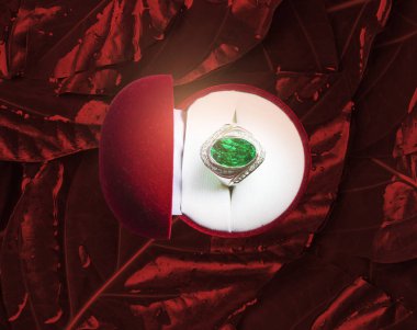 Zümrüt yeşili değerli taş yüzük. Kırmızı arka plan parlak kırmızıdır. Yeşil değerli taşlara odaklanın