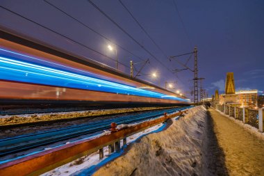 Karanlıkta demiryolu köprüsünün arka planında hareket bulanıklığı olan yüksek hızlı tren