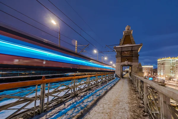 Высокоскоростной поезд с размытым движением на фоне железнодорожного моста в темноте — стоковое фото