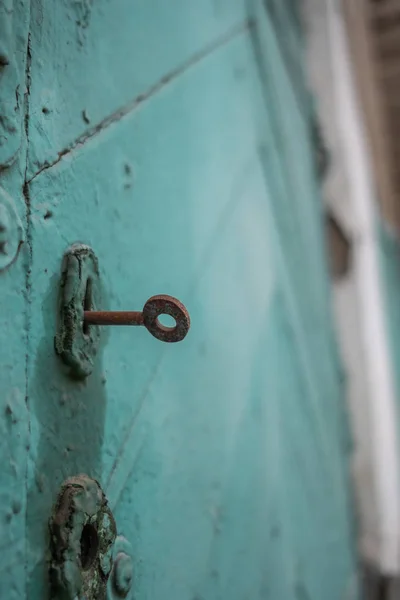 Staré dřevěné dveře vybarvené prasklou zelenou barvou. Rusty klíč v klíčové dírce. — Stock fotografie