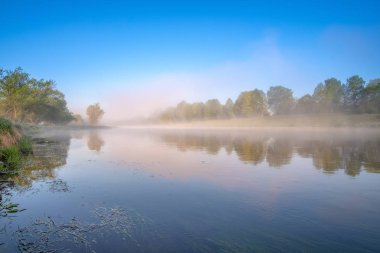 Красочный вид на реку, окутанную туманом, ползущим над водой. Рассвет прохладное утро. Трава с каплей росы и тумана над водой, как вата .