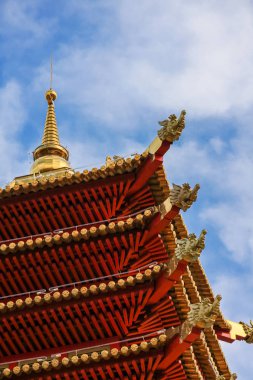 Pagoda kırmızı çok seviyeli çatı köşesi, altın ile dekore, açık beyaz bulutlar ile mavi gökyüzüne karşı.