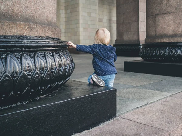 Ein kleines Mädchen sitzt auf dem Sockel einer massiven Granitsäule, auf der ihre Hand ruht. ein monumentales Gebäude in Moskau — Stockfoto