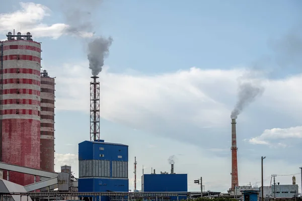 Vista de un complejo de edificios industriales con chimeneas humeantes en la tarde contra el cielo con nubes . — Foto de Stock