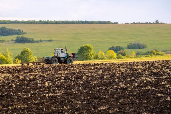 Un tractor agrícola arada un campo con un arado después de cosechar trigo en los rayos del sol de la noche . —  Fotos de Stock