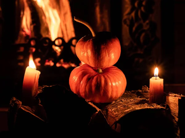 Две хэллоуинские тыквы в темноте на березовых бревнах, горящих свечами. На заднем плане - пламя от камина . — стоковое фото