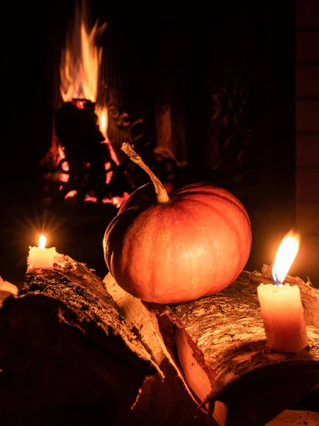 Хэллоуинская тыква в темноте на березовых бревнах рядом с горящими свечами. На заднем плане - пламя от камина . — стоковое фото