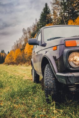 Islak bir sonbahar gününde, Rus kırsalında, bir ormanın kenarında solmuş çimenler üzerinde bir jipin tekerlekleri..