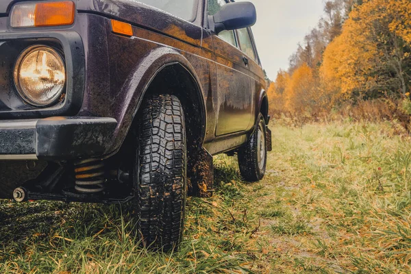 Ruedas de un SUV sobre hierba húmeda y descolorida en el borde de un bosque en el interior ruso en un día nublado de otoño . — Foto de Stock