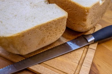 Taze pişmiş ev yapımı ekmek. Tahta bir mutfak tahtasında ikiye bölünmüş. Ekmek kesmek için ekmek bıçağının yanında yatıyor..