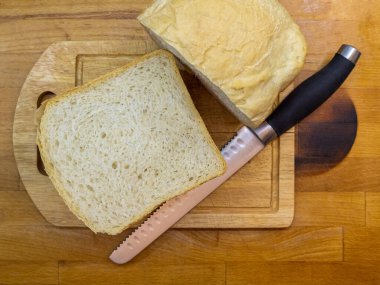 Taze pişmiş ev yapımı ekmek. Tahta bir mutfak tahtasında ikiye bölünmüş. Ekmek kesmek için ekmek bıçağının yanında yatıyor..
