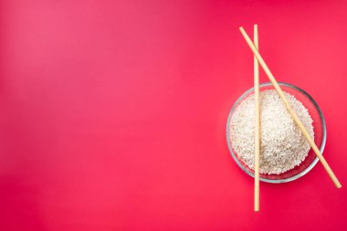 Düz yatıyordu. Pembe arka planda pilav ve çubuklarla şeffaf cam kase..