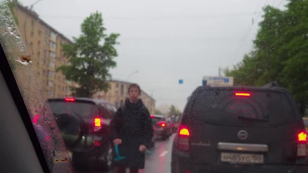 モスクワ ロシア 2020年6月8日 街中の渋滞で車のフロントガラスに雨滴に選択的な焦点を当てます 車のジェスチャーの間を歩く10代の若者 ヘッドライトを洗うために提供します — ストック動画